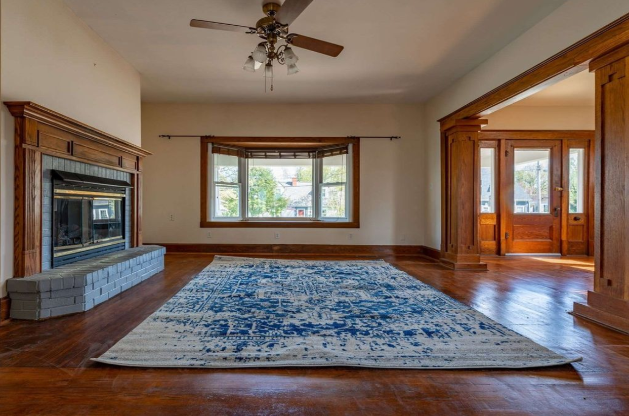An empty living room with a fireplace , rug and ceiling fan.