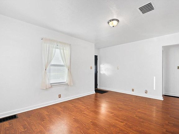 An empty living room with hardwood floors and white walls.