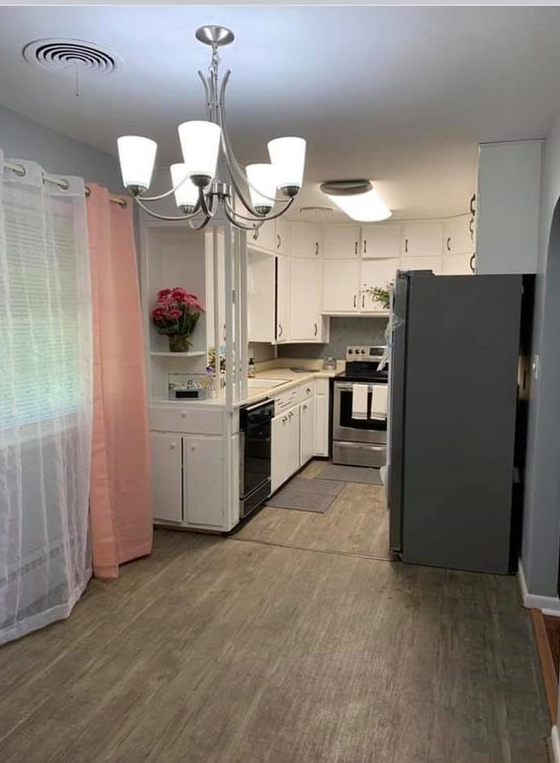 A kitchen with white cabinets , stainless steel appliances , a refrigerator and a chandelier.