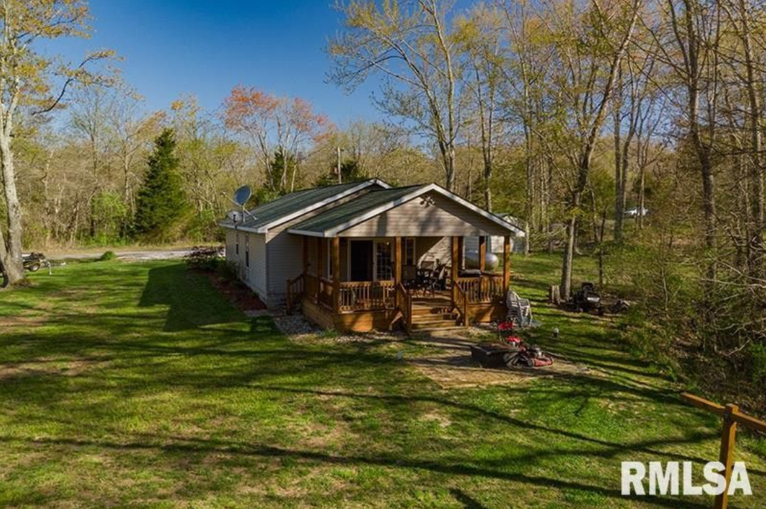 A small house is sitting in the middle of a lush green field surrounded by trees.