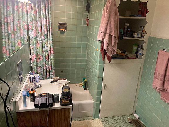 A bathroom with green tiles , a sink , a bathtub and a shower curtain.
