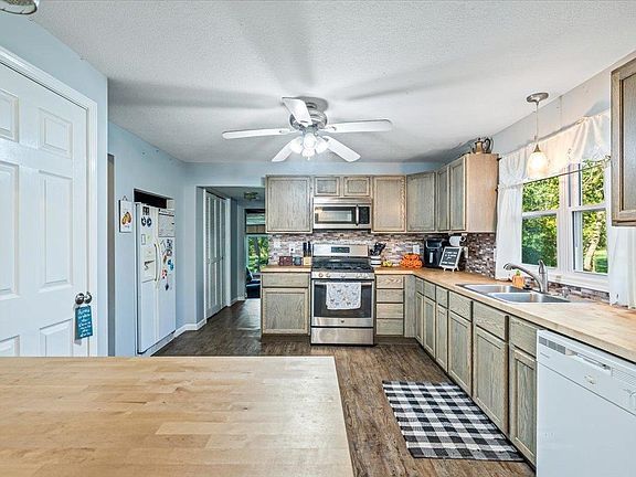 A kitchen with stainless steel appliances , wooden cabinets , a ceiling fan and a wooden table.