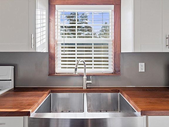 A kitchen with a stainless steel sink and a window with blinds.