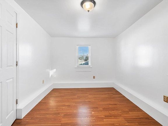 An empty room with hardwood floors , white walls and a window.