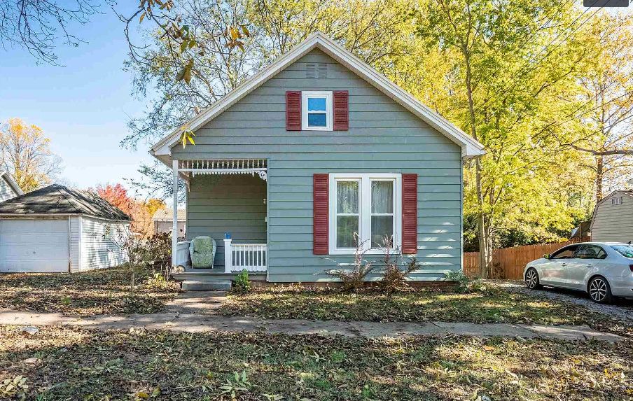 A small house with red shutters and a car parked in front of it.