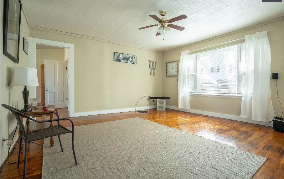 An empty living room with a ceiling fan and a chair.