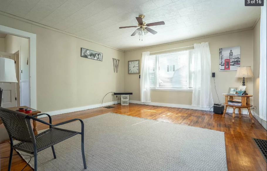 An empty living room with a ceiling fan and a chair.