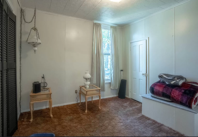 An empty room with a blanket on a bench and a lamp on a table.