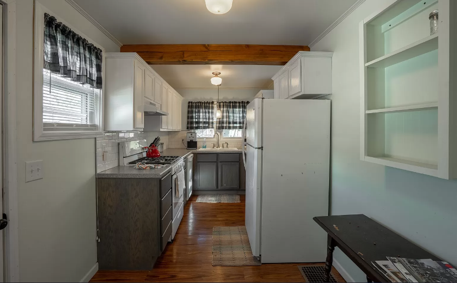A kitchen with white cabinets , a refrigerator , a stove , and a window.