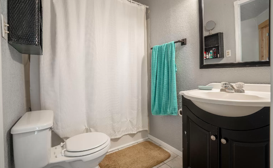 A bathroom with a toilet , sink , mirror and shower curtain.