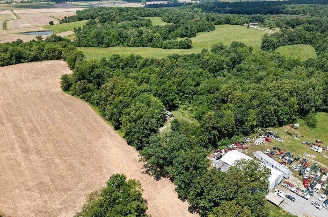 An aerial view of a field surrounded by trees and a parking lot.