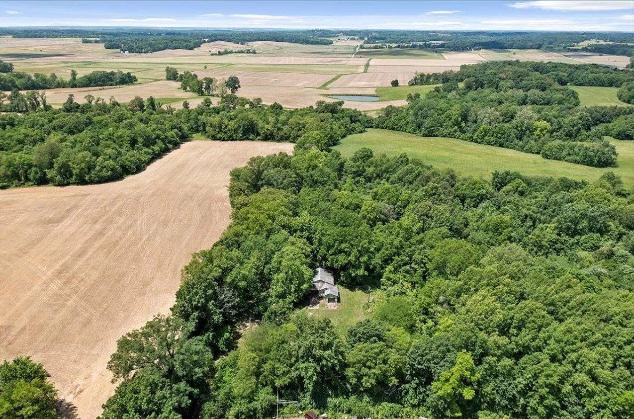 An aerial view of a house in the middle of a lush green forest surrounded by fields.