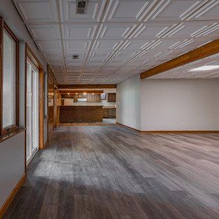 A large empty room with hardwood floors and a ceiling tile.