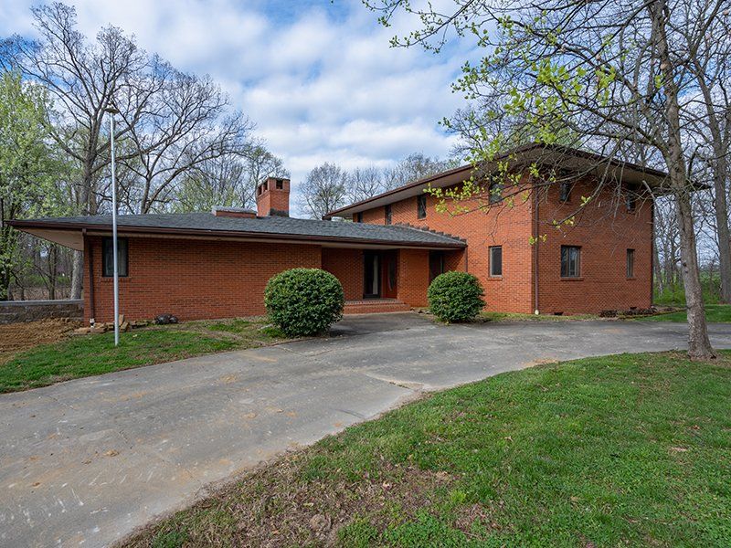 A large red brick house with a driveway and trees in the background.