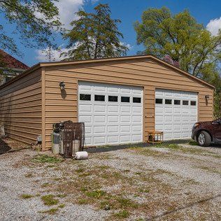 A car is parked in front of a garage with two garage doors.