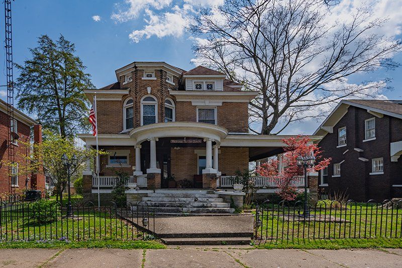 A large brick house with a porch and a fence in front of it.