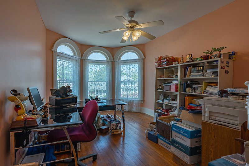 A room with a desk , chair , computer and a ceiling fan.