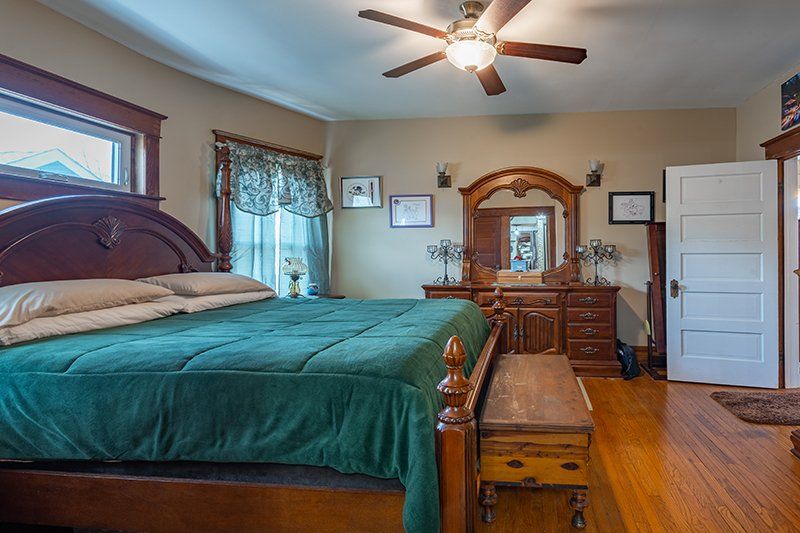 A bedroom with a king size bed , dresser , mirror and ceiling fan.