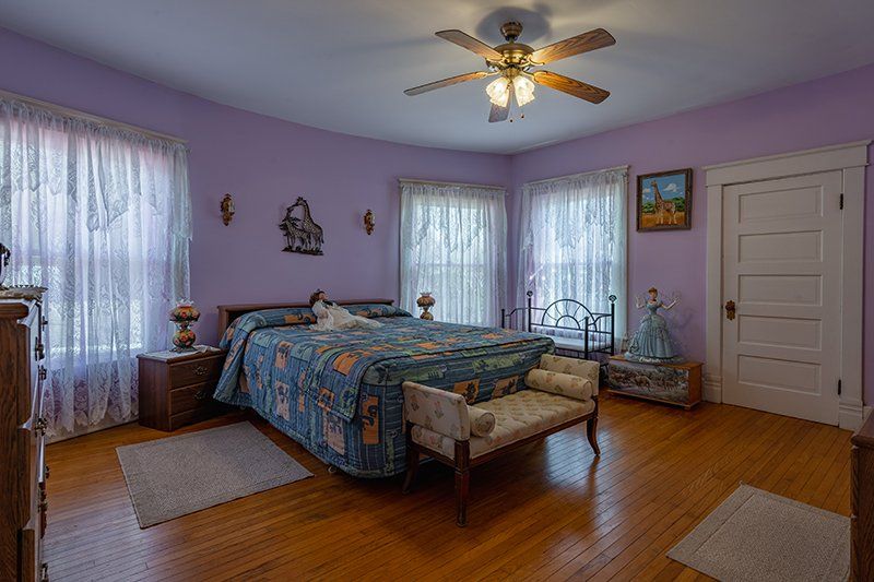 A bedroom with purple walls , a bed , a bench and a ceiling fan.