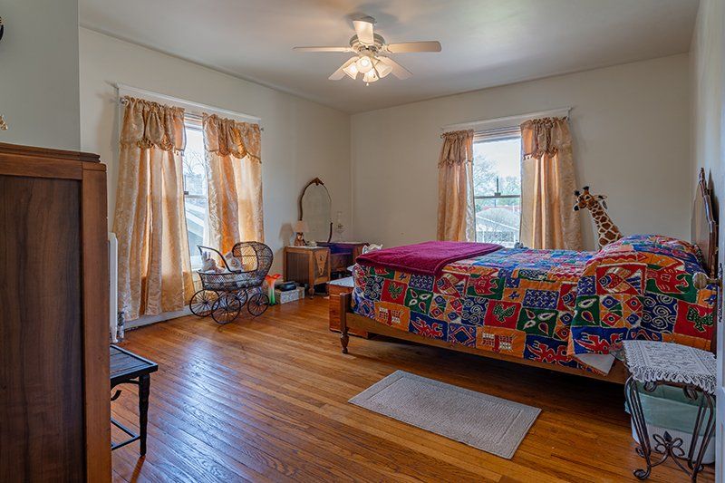 A bedroom with hardwood floors , a bed and a ceiling fan.
