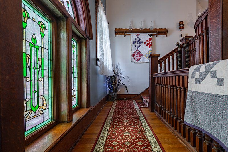 A hallway with stained glass windows and a quilt on the railing.