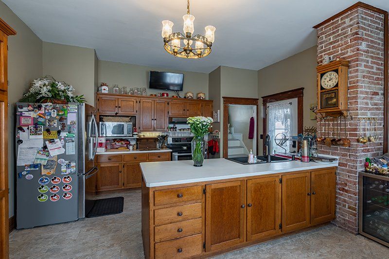 A kitchen with wooden cabinets , a refrigerator , a clock and a large island.