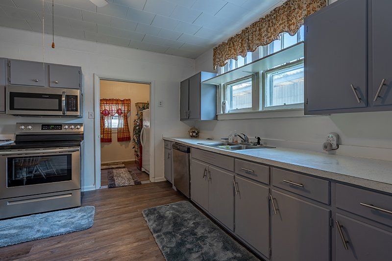 A kitchen with gray cabinets , a stove , a microwave , and a sink.