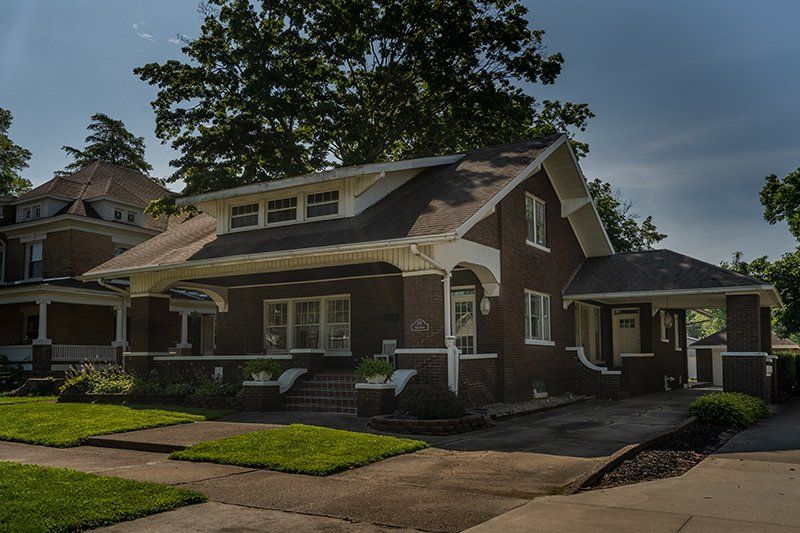 A brick house with a gray roof and a white trim is sitting on a lush green lawn.