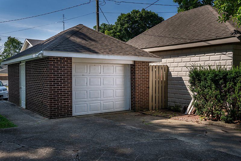 A white car is parked in a garage next to a brick house.