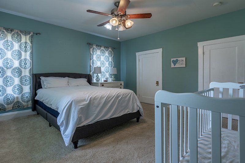 A bedroom with a bed , crib and ceiling fan.