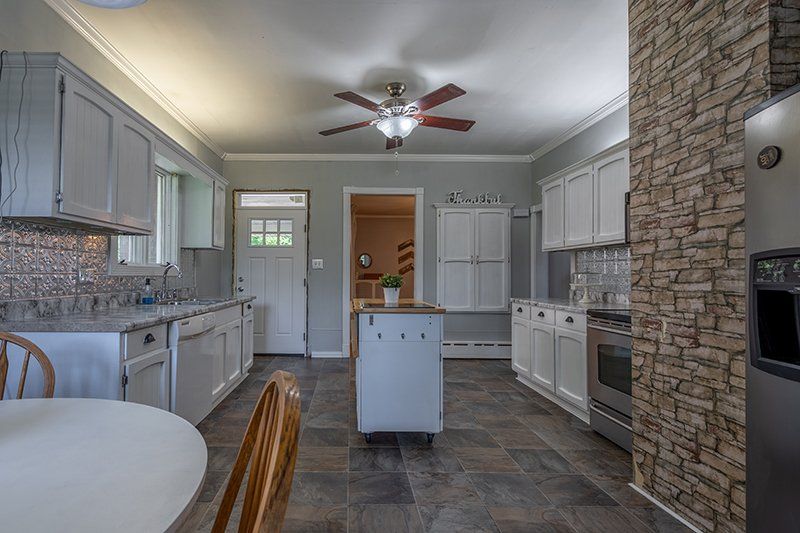 A kitchen with white cabinets , stainless steel appliances and a ceiling fan.