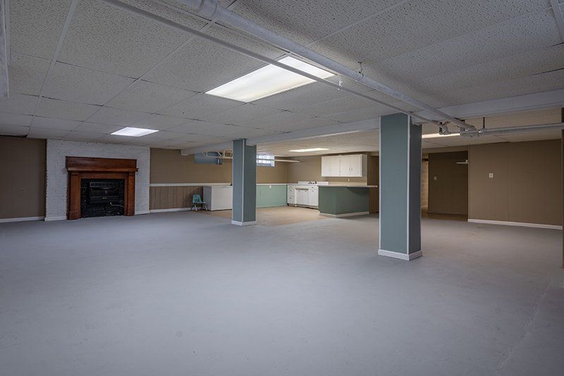 An empty basement with a fireplace and a kitchen.