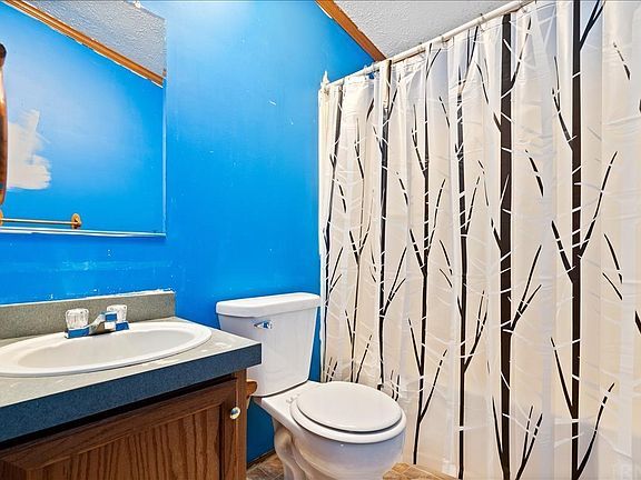A bathroom with a toilet a sink and a shower curtain with trees on it