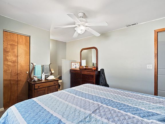 A bedroom with a bed , dresser , mirror and ceiling fan.