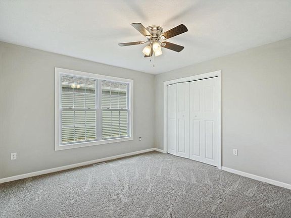 An empty bedroom with a ceiling fan and two windows.
