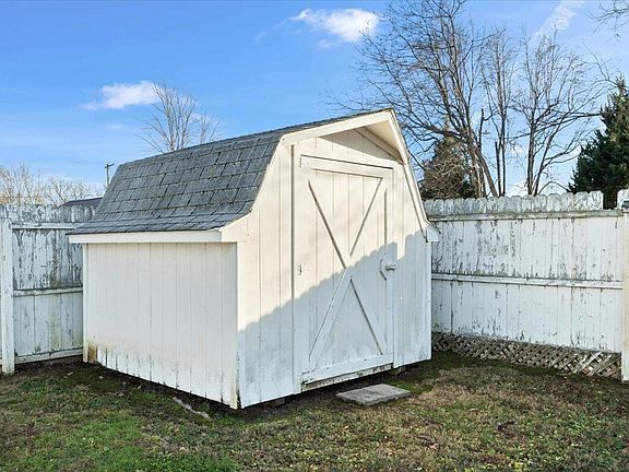 A white shed is sitting in the grass next to a white fence.
