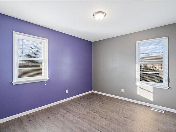 An empty room with purple walls and two windows.