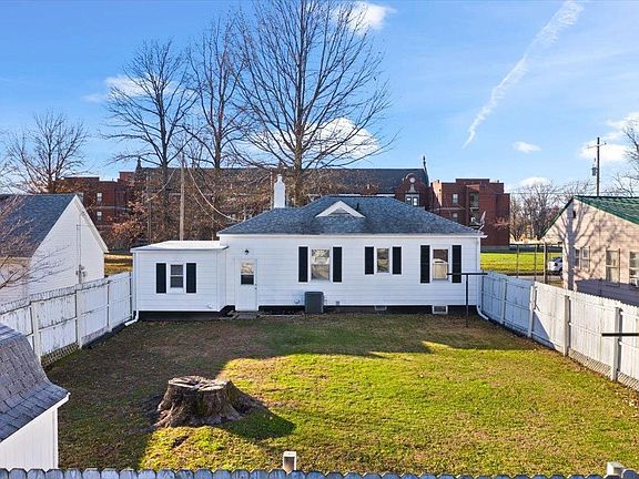 The backyard of a white house with a white fence and a stump in the middle of it.
