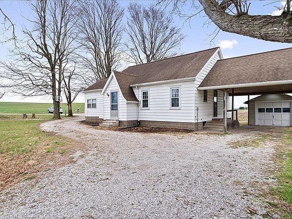 A white house with a brown roof is sitting in the middle of a grassy field.