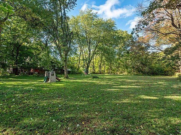 A large lush green field surrounded by trees on a sunny day.