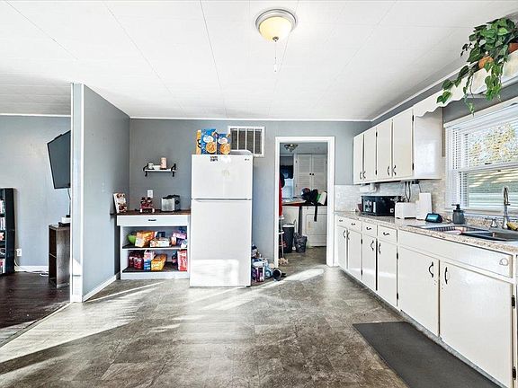 A kitchen with white cabinets , a refrigerator , a sink , and a window.