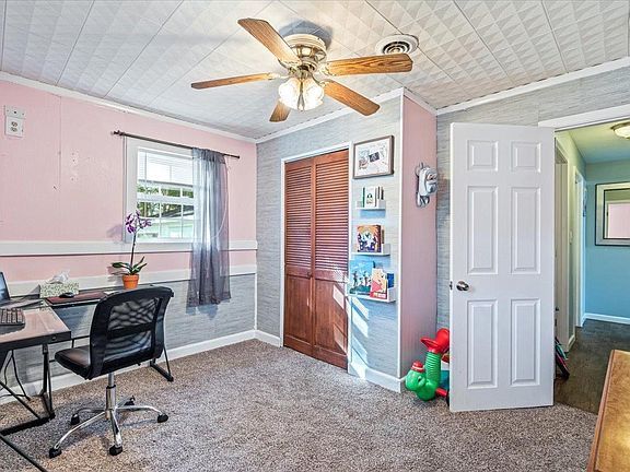 A bedroom with a desk , chair and ceiling fan.