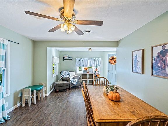 A dining room with a long wooden table and chairs and a ceiling fan.