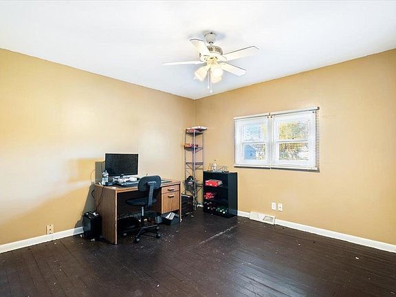 A room with a desk , chair , computer and ceiling fan.