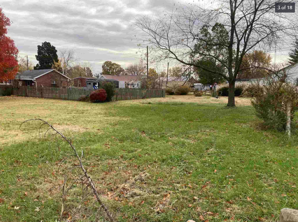 A large grassy field with a barbed wire fence and a house in the background.