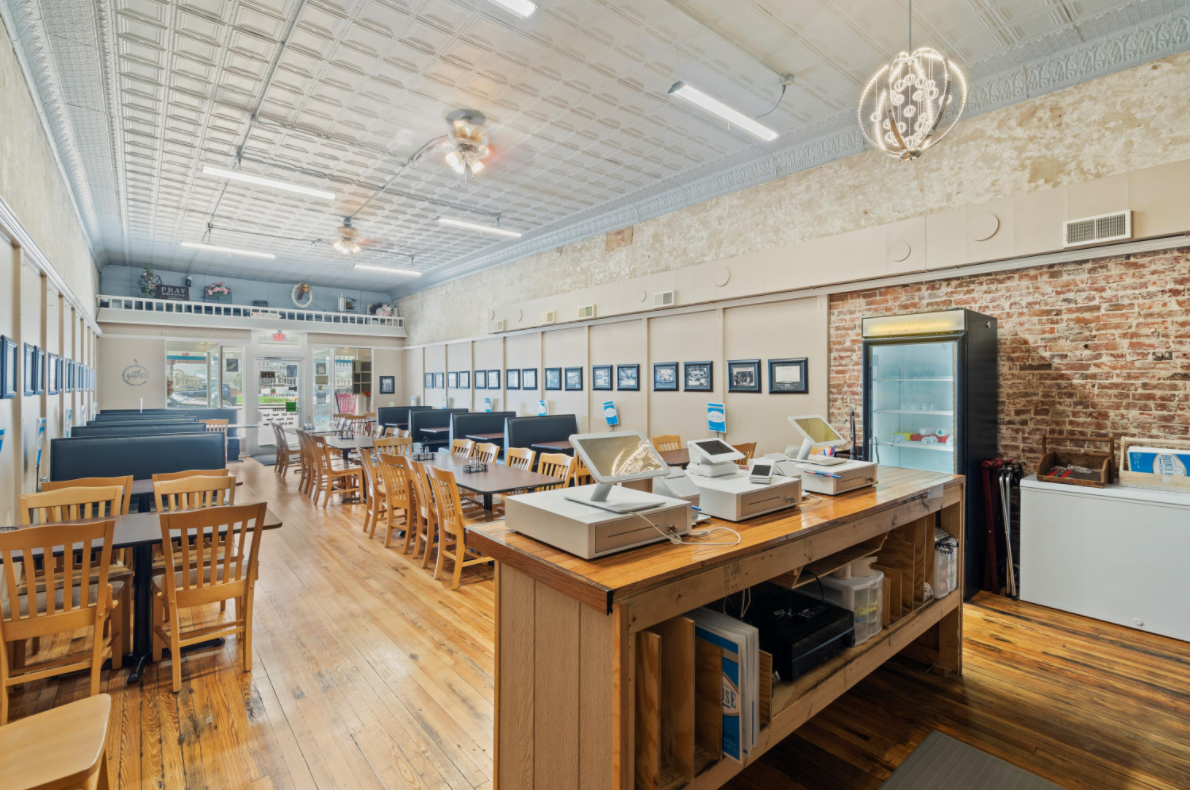 A large room with tables and chairs and a long wooden table in the middle of the room.