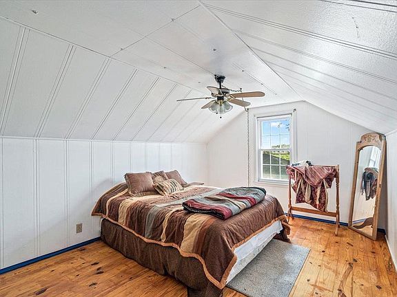 A bedroom with a bed , ceiling fan , mirror and window.