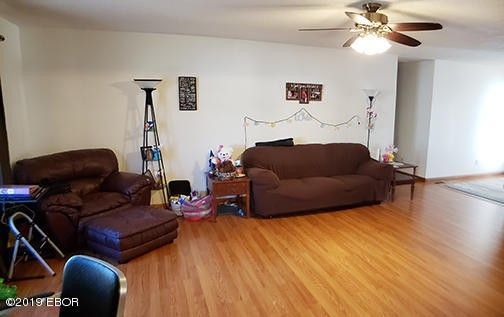 A living room with a couch , chair , ottoman and ceiling fan.