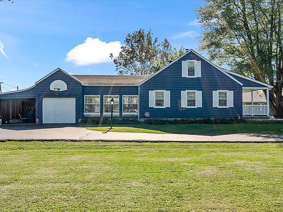 A large blue house with white shutters is sitting on top of a lush green field.