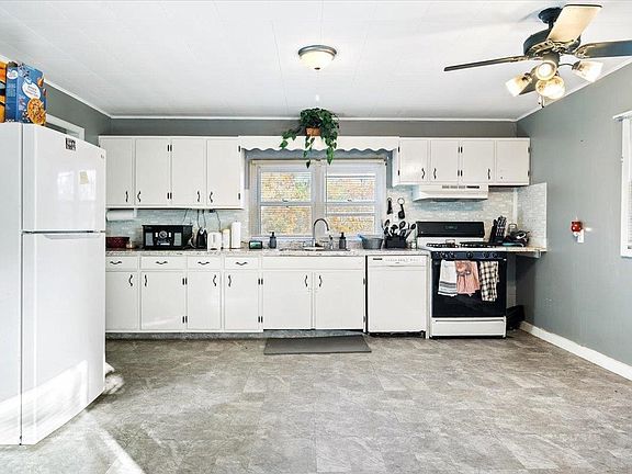 A kitchen with white cabinets , a refrigerator , a stove , and a ceiling fan.
